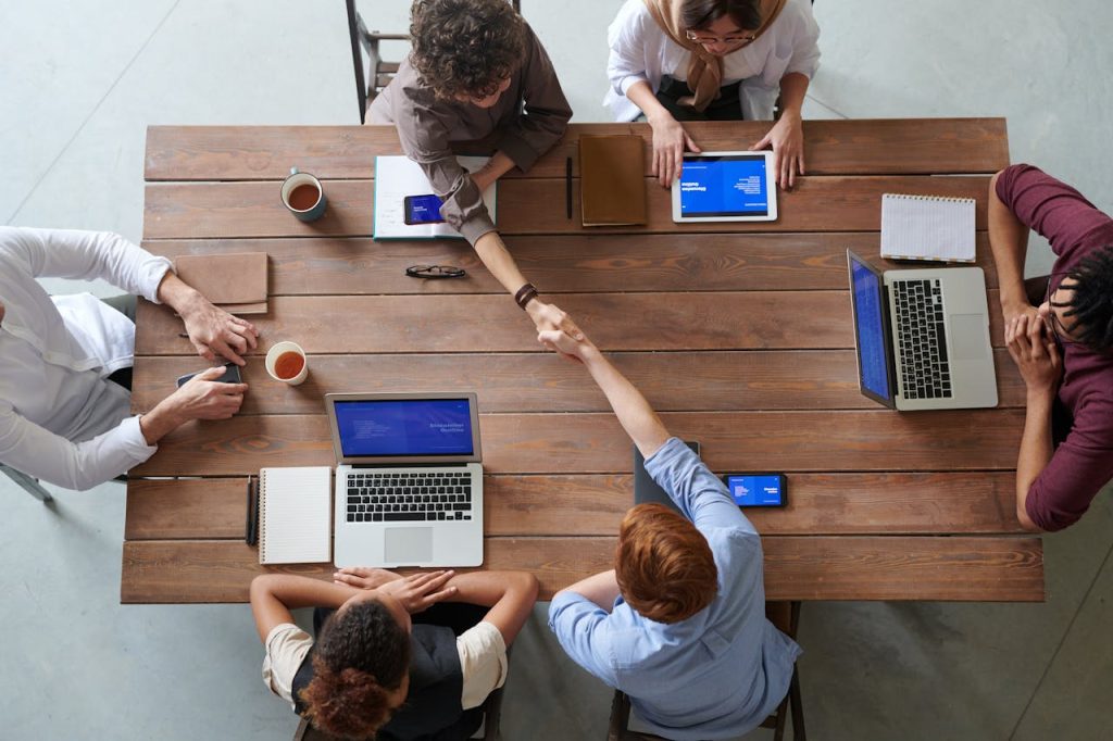 Overhead view of colleagues in a work meeting using laptops and tablets, emphasizing teamwork and technology.
